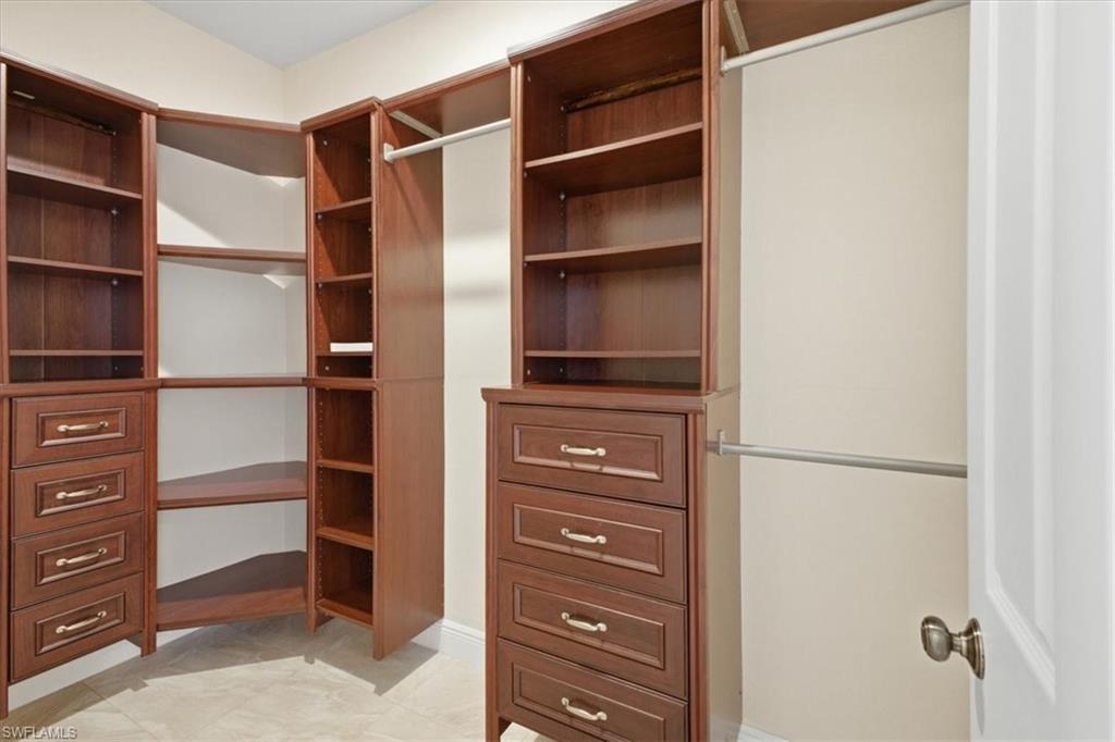 Custom closet system featuring rich wood-finish cabinetry, built-in shelving, multiple hanging rods, and integrated drawer storage with brushed metal hardware