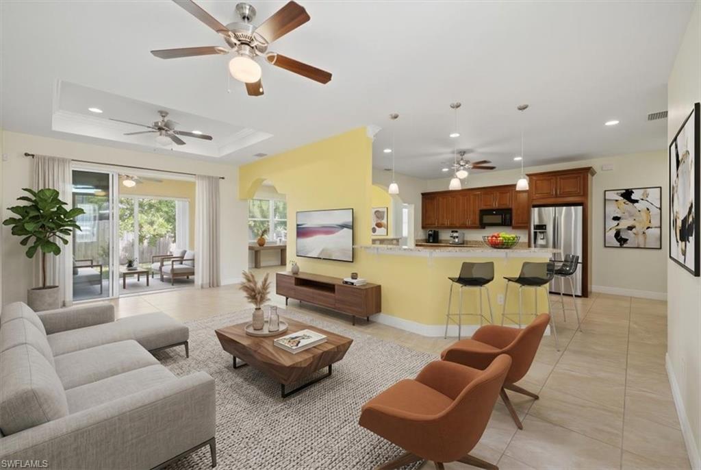 Open-concept living area featuring light-toned tile flooring, tray ceilings with ceiling fans, and sliding glass doors opening to an outdoor patio