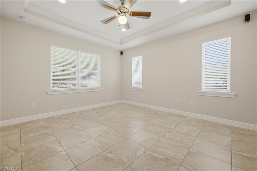Spacious interior room featuring light-toned tile flooring, tray ceiling with recessed lighting, and a ceiling fan