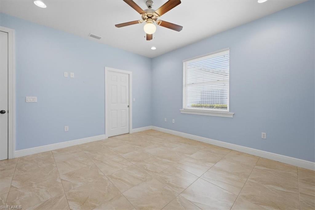 Spacious room featuring neutral tile flooring, light blue walls, and a ceiling fan with integrated lighting