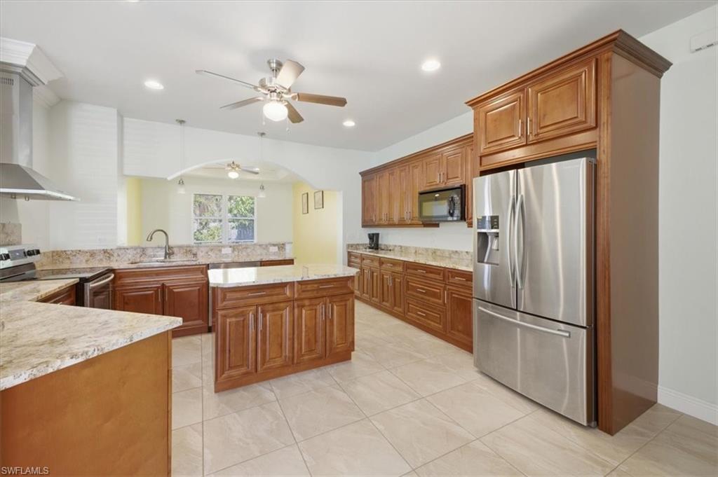 Spacious kitchen featuring a central island, wood cabinetry, light-toned granite countertops, stainless steel appliances, and tile flooring