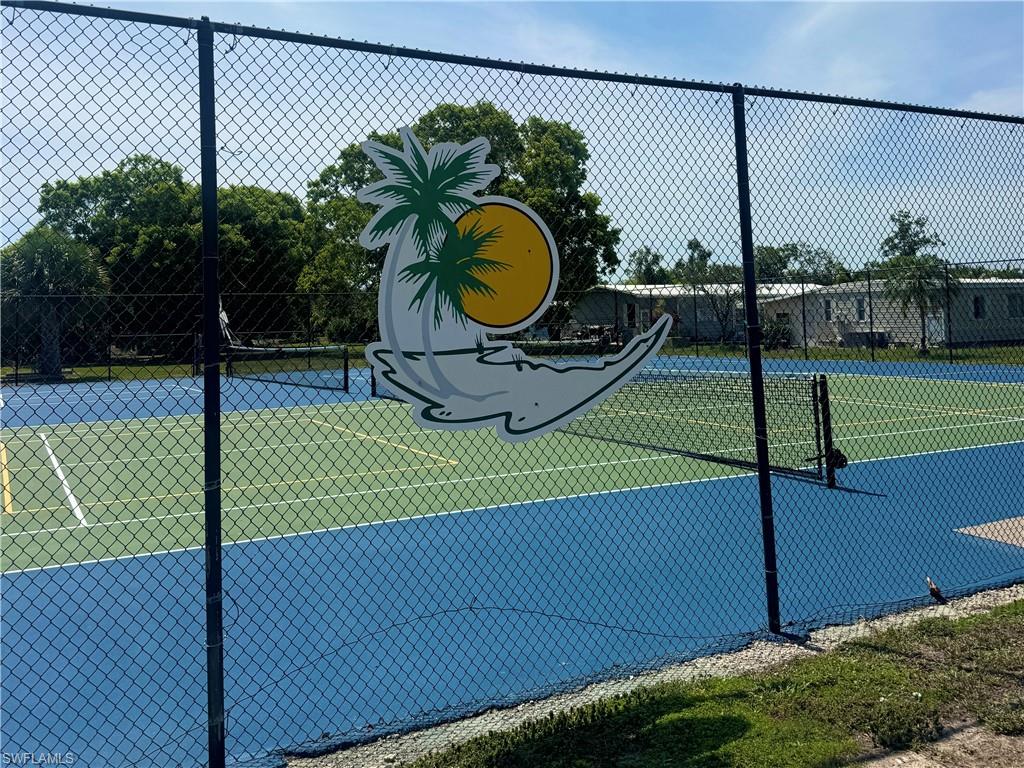 Fenced tennis court featuring a blue playing surface with green court lines and a net