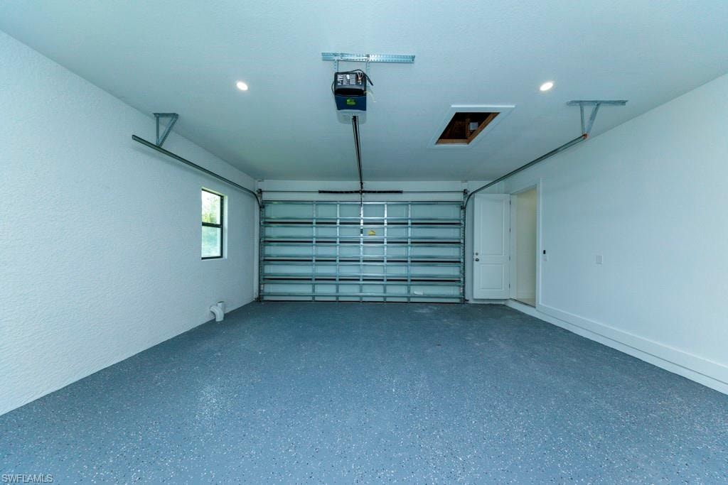 Spacious garage featuring an epoxy-coated floor, automatic garage door opener, recessed lighting, and a side entry door