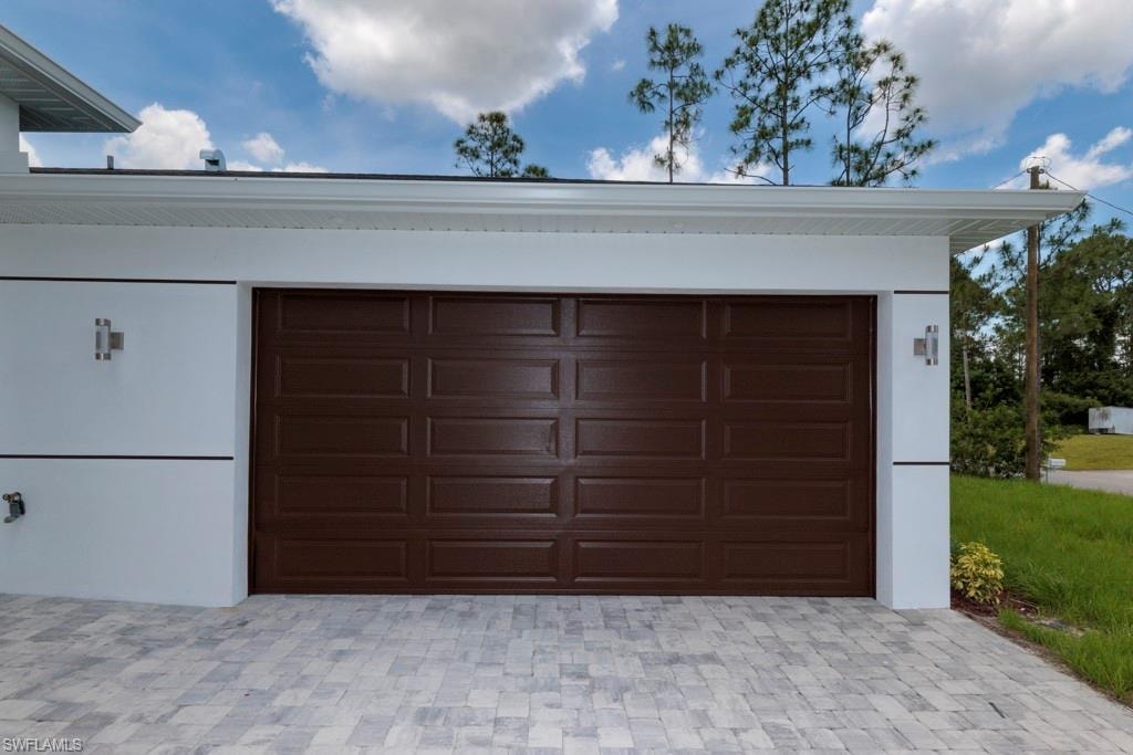 Garage entry featuring a paneled brown door and a light-toned paver driveway