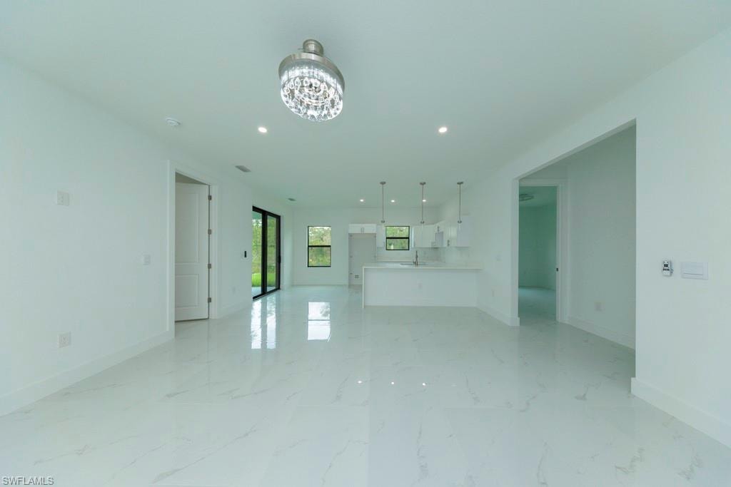 Spacious open-concept living area featuring large format white tile flooring, recessed lighting, and a modern chandelier