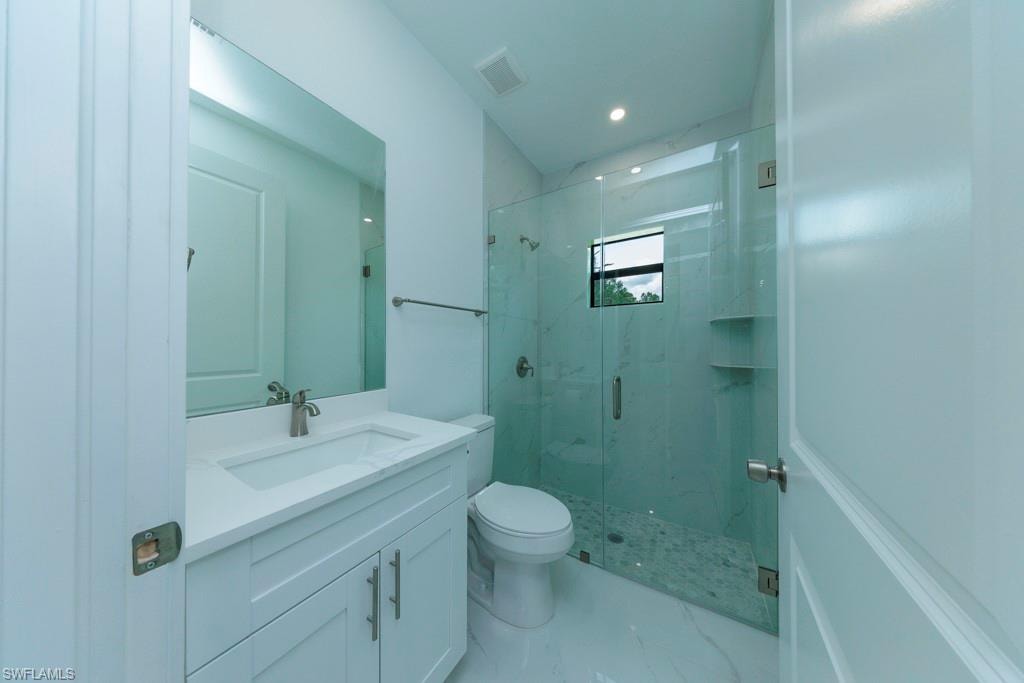 Bathroom featuring a white vanity with integrated sink, brushed nickel faucet, large mirror, and glass-enclosed shower with tiled walls and pebble-finish floor
