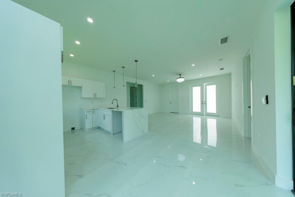 Open-concept interior featuring white-finish cabinetry, a waterfall island, pendant lighting, recessed lighting, and French doors