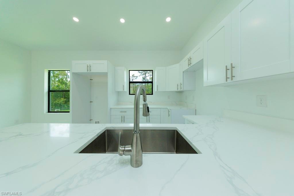 Kitchen featuring a large undermount stainless steel sink with a brushed nickel pull-down faucet, white shaker-style cabinetry, and white countertops with subtle veining