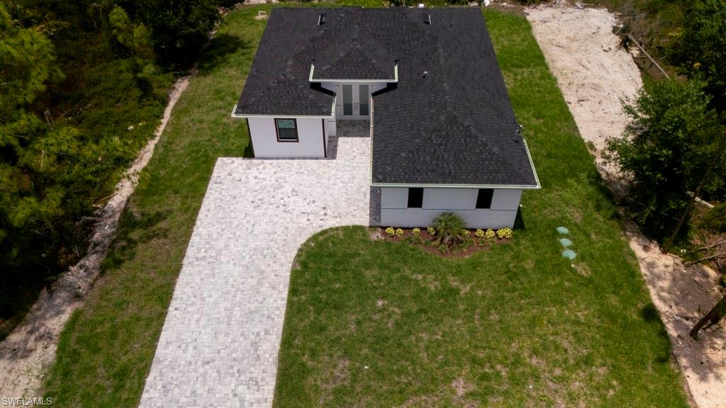 New construction residence featuring a black shingle roof, white exterior siding, and an expansive paver driveway