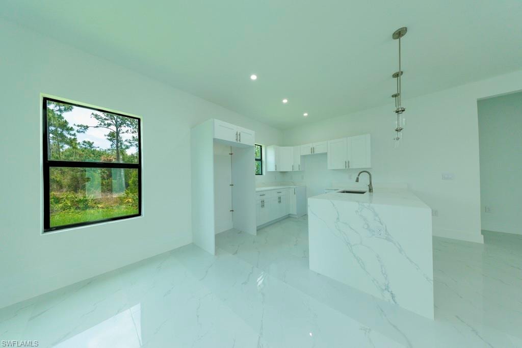 Modern kitchen featuring a waterfall island with a veined countertop, stainless steel sink and faucet, white cabinetry, recessed lighting, and large format tile flooring