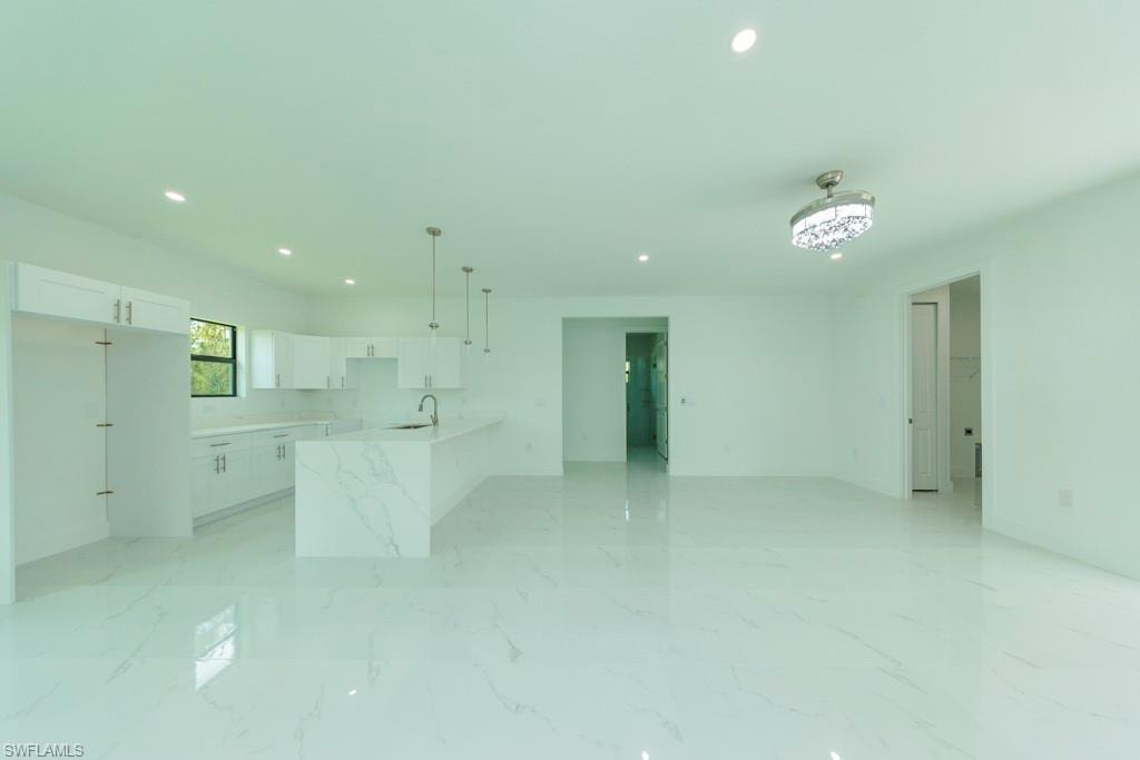Open-concept living area featuring large format white tile flooring with subtle veining, recessed lighting, and a modern chandelier