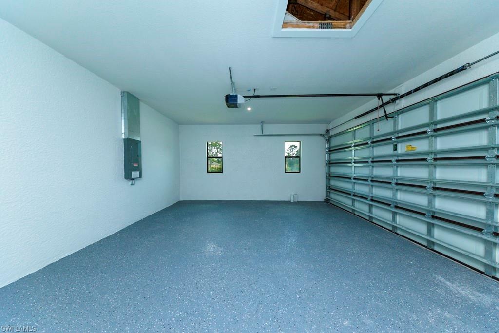 Spacious garage featuring a durable, speckled epoxy floor finish, an automatic garage door opener, two windows providing natural light, and an attic access hatch