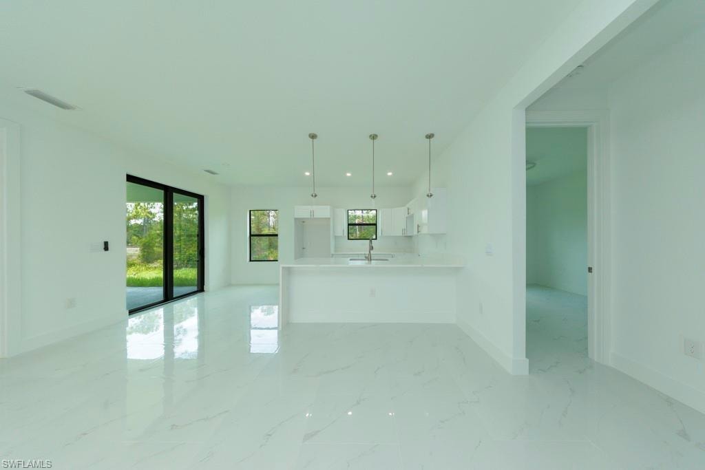 Open-concept living area featuring large format white tile flooring, a kitchen island with pendant lighting, white cabinetry, and a sliding glass door leading to the exterior