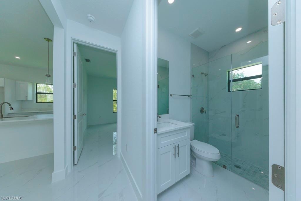 Contemporary bathroom featuring a glass-enclosed shower with tiled walls, a single vanity with a white cabinet, and recessed lighting