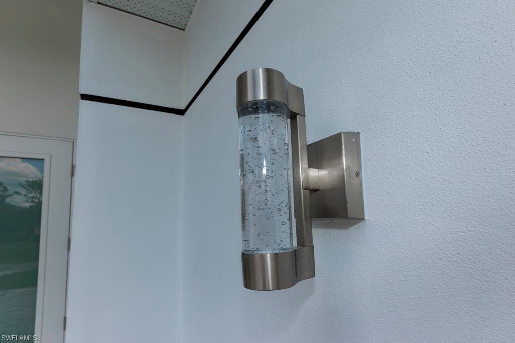 Brushed nickel wall sconce with a clear, cylindrical glass housing featuring internal bubble details, mounted on a white textured exterior wall