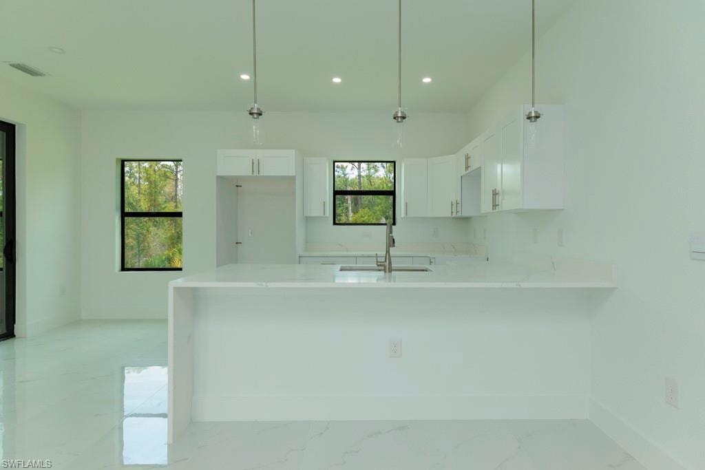 Bright kitchen area featuring white cabinetry and countertops, a built-in sink, stainless steel faucet, and recessed lighting