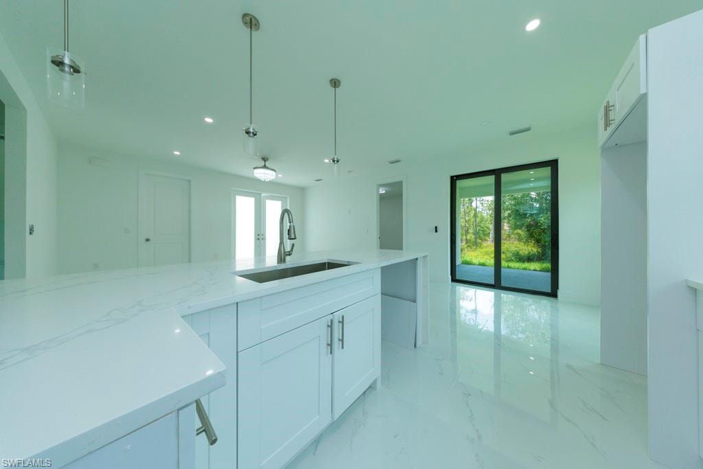 Kitchen island featuring a stainless steel sink, a gooseneck faucet, and quartz countertops with white cabinetry