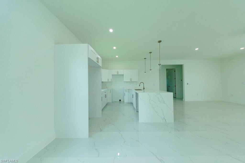 Open-concept kitchen featuring an oversized island with waterfall-edge countertop, white shaker-style cabinetry, a stainless steel sink with gooseneck faucet, and recessed lighting