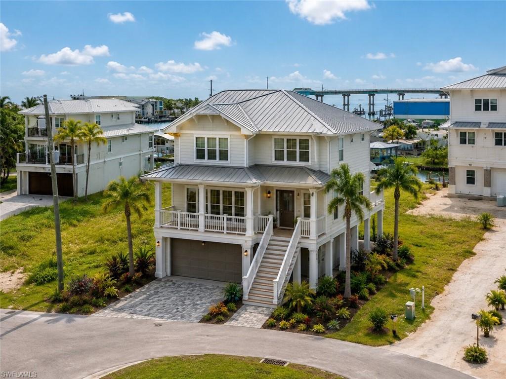 AI Rendering - Elevated coastal residence featuring a metal roof, front balcony, covered entry porch, paver driveway, and mature palm trees - Virtually Edited Image