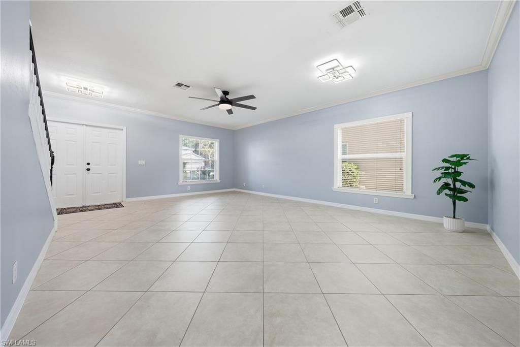 Spacious interior featuring light-colored tile flooring, light blue walls, white baseboards, and crown molding