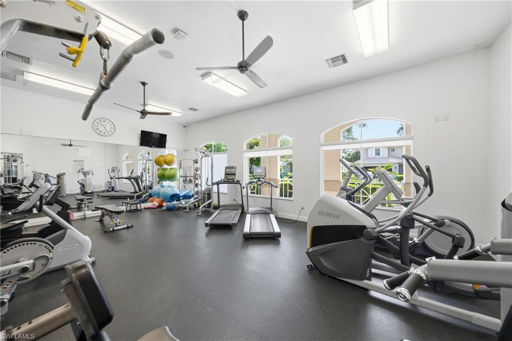 Fitness center featuring ample natural light from arched windows, dark rubber flooring, and multiple ceiling fans