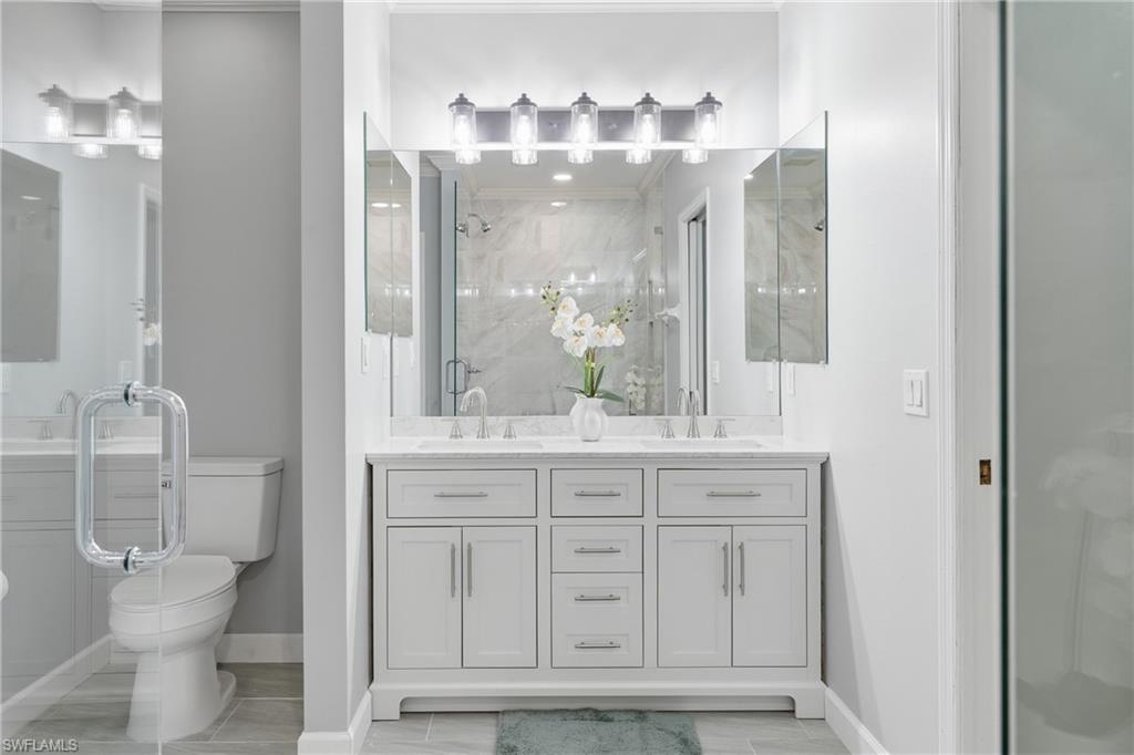 Dual vanity with white cabinetry and integrated sinks, complemented by a large mirror and multi-bulb fixture