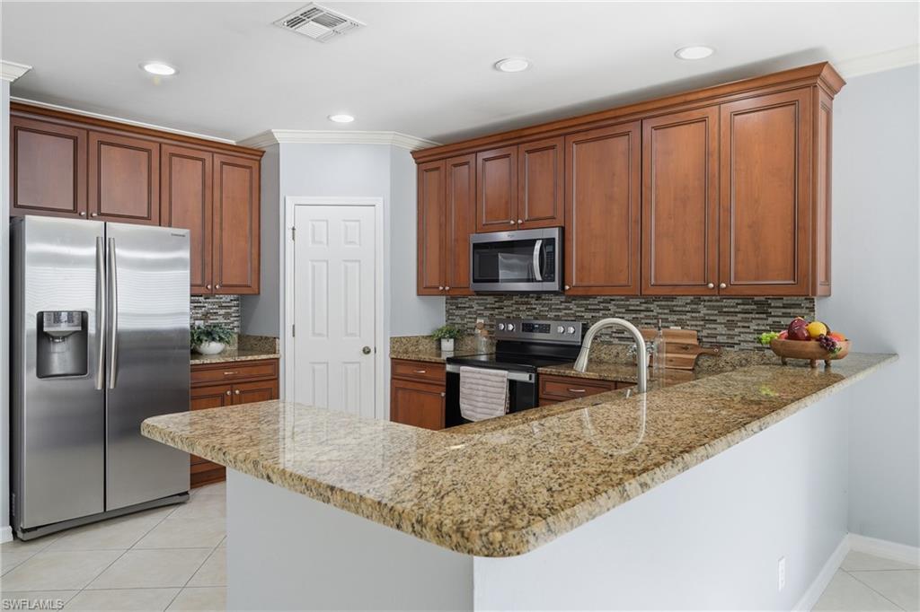 Kitchen featuring a U-shaped countertop with a raised bar, wood cabinetry, stainless steel appliances, and tile flooring