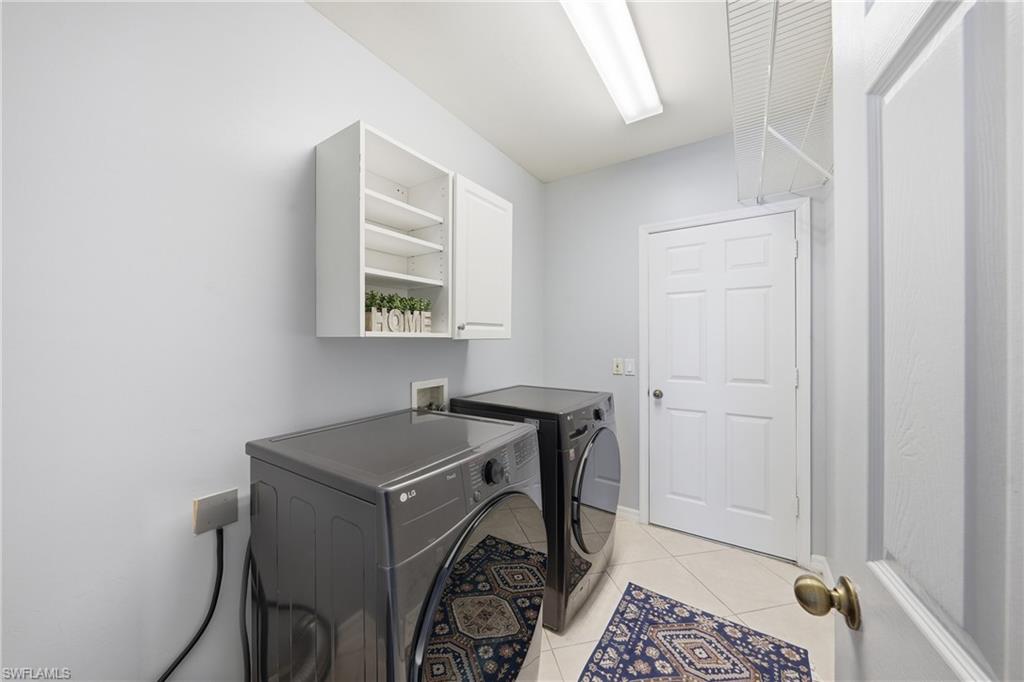 Dedicated laundry area featuring tile flooring, overhead fluorescent lighting, white cabinetry, and a white six-panel door