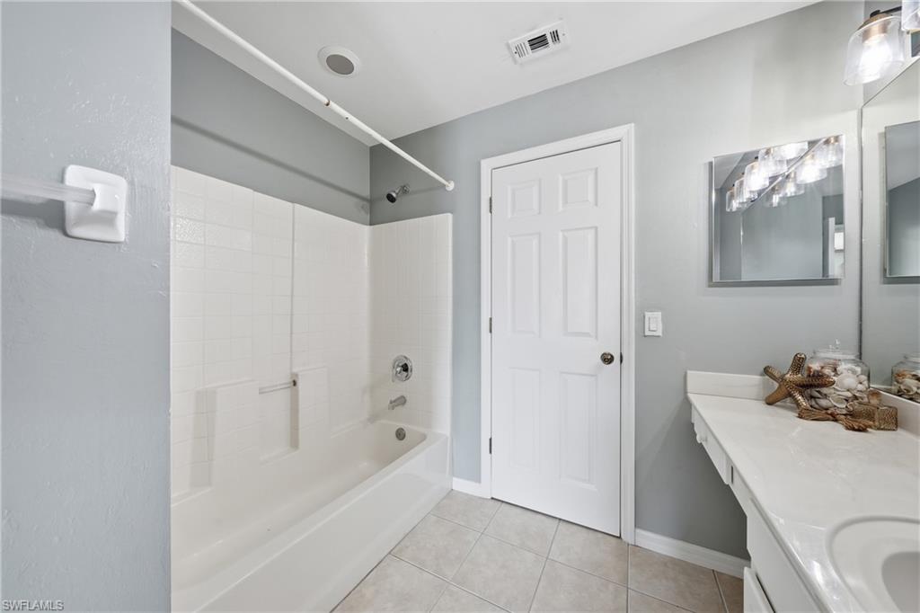 Full bathroom featuring a white tub and shower combination with a tiled surround, a built-in vanity with an integrated sink, a large wall mirror, and neutral-toned floor tiling