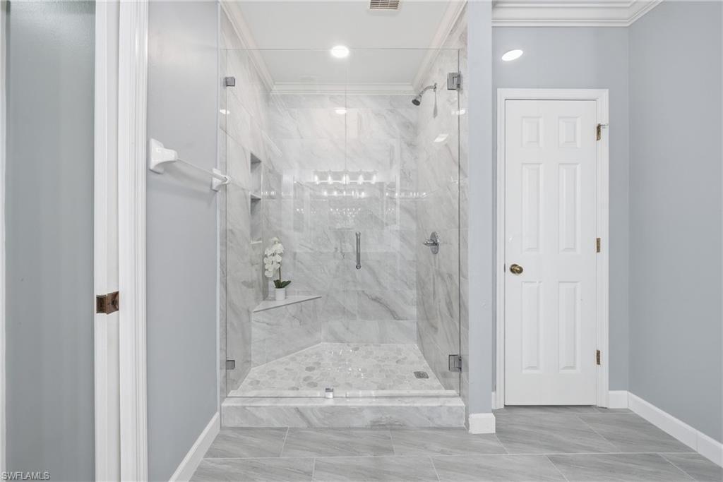 Frameless glass shower enclosure featuring marble-look tile walls, a built-in corner bench, and dual recessed shelves
