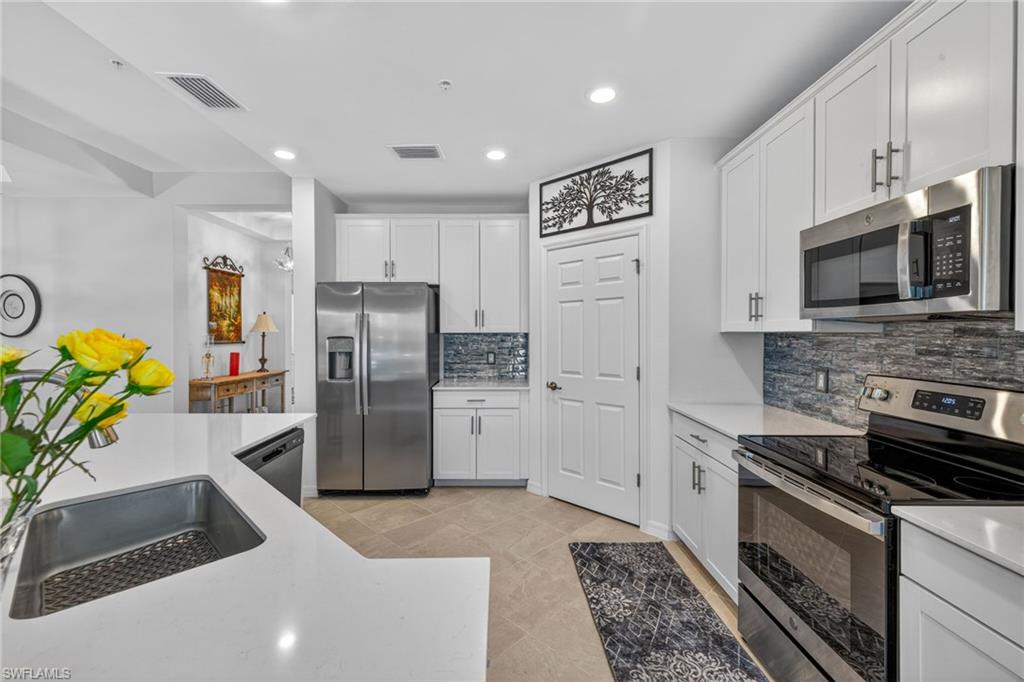 Contemporary kitchen featuring white cabinetry, stainless steel appliances, a white solid surface countertop, an undermount sink, and tile flooring