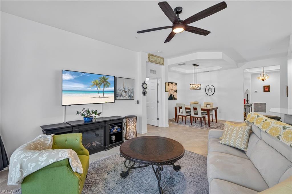 Open-concept living area featuring a ceiling fan with integrated lighting, tray ceiling, tile flooring, and white walls
