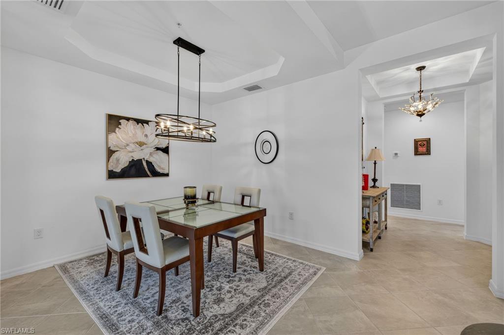Dining space featuring tray ceiling, contemporary chandelier, tile flooring, and arched entryway with decorative lighting