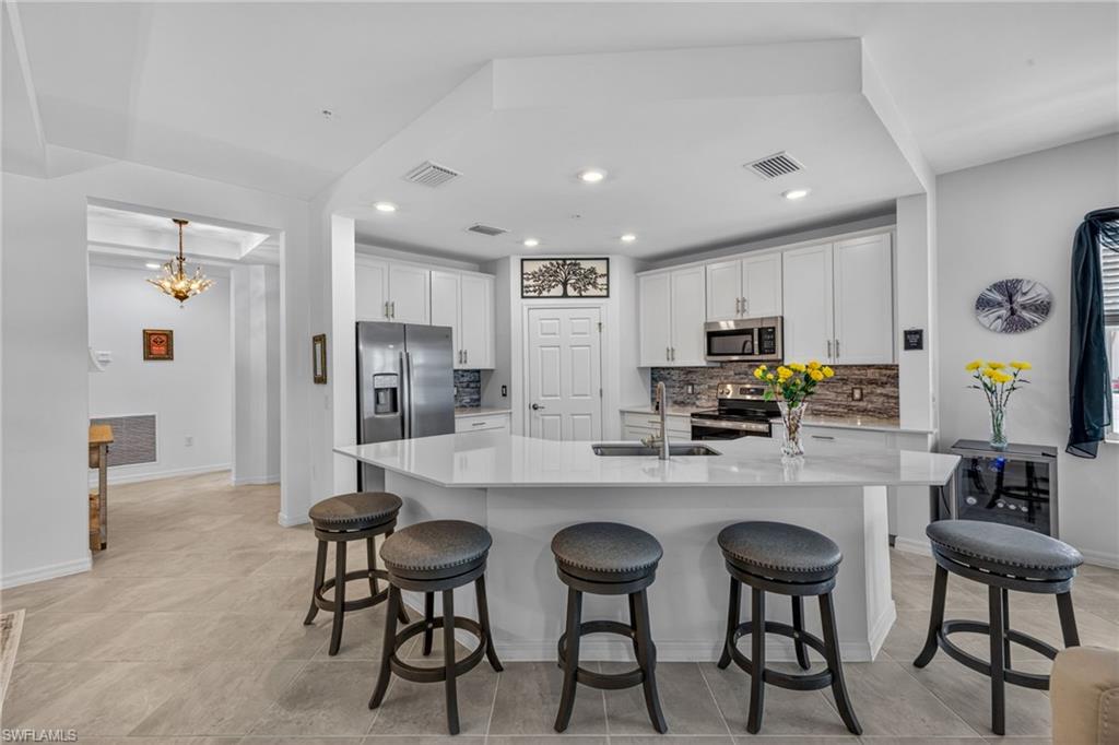 Kitchen featuring a central island with countertop seating, white cabinetry, stainless steel appliances, and a tiled backsplash