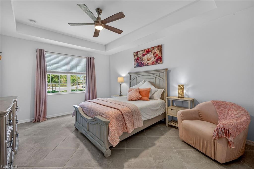 Spacious room featuring tray ceilings with a ceiling fan, large window with blinds, and durable tile flooring