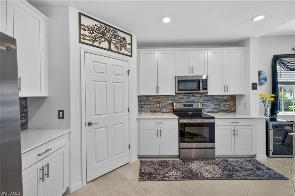Contemporary kitchen featuring white shaker cabinetry, stainless steel appliances, stacked stone-look backsplash, and recessed lighting