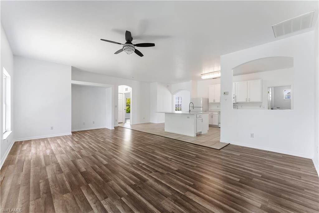 Expansive living area with wood-finish flooring, a decorative ceiling fan, and abundant natural light from multiple windows