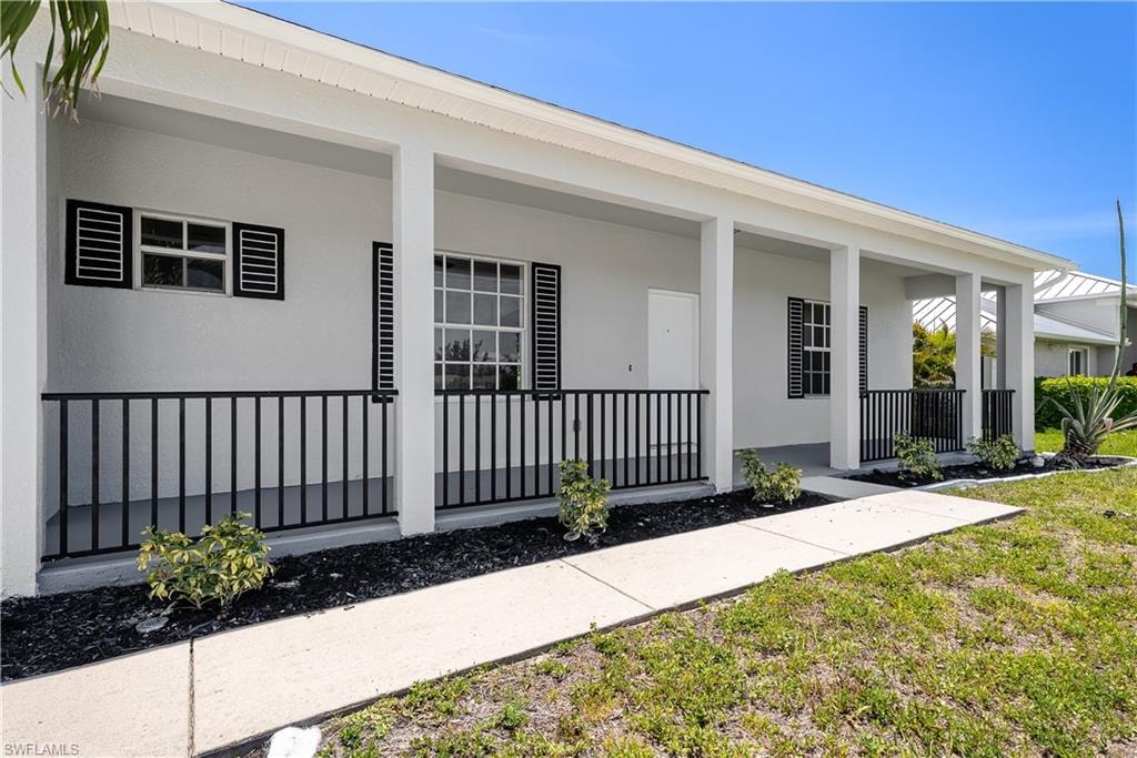 Modern ranch-style home featuring a covered front porch with black iron railings, white exterior walls, multiple windows with black louvered shutters, and a concrete walkway