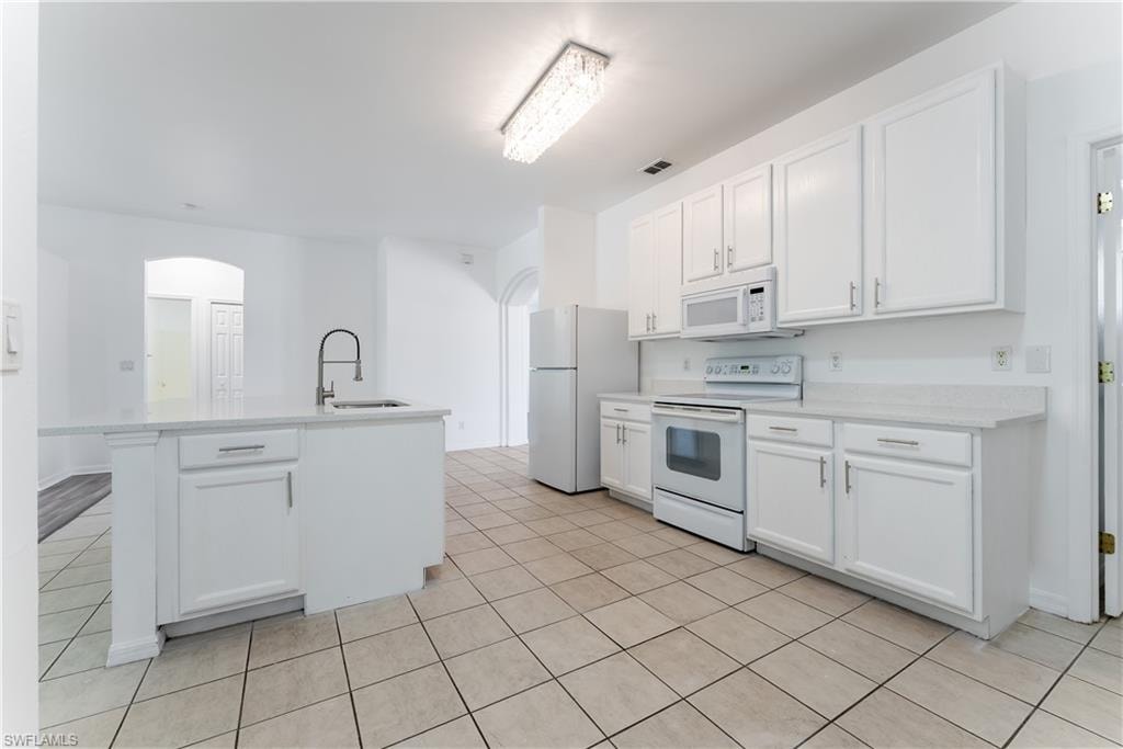 Kitchen featuring an island with an integrated sink, white cabinetry, white appliances, and light-toned countertops