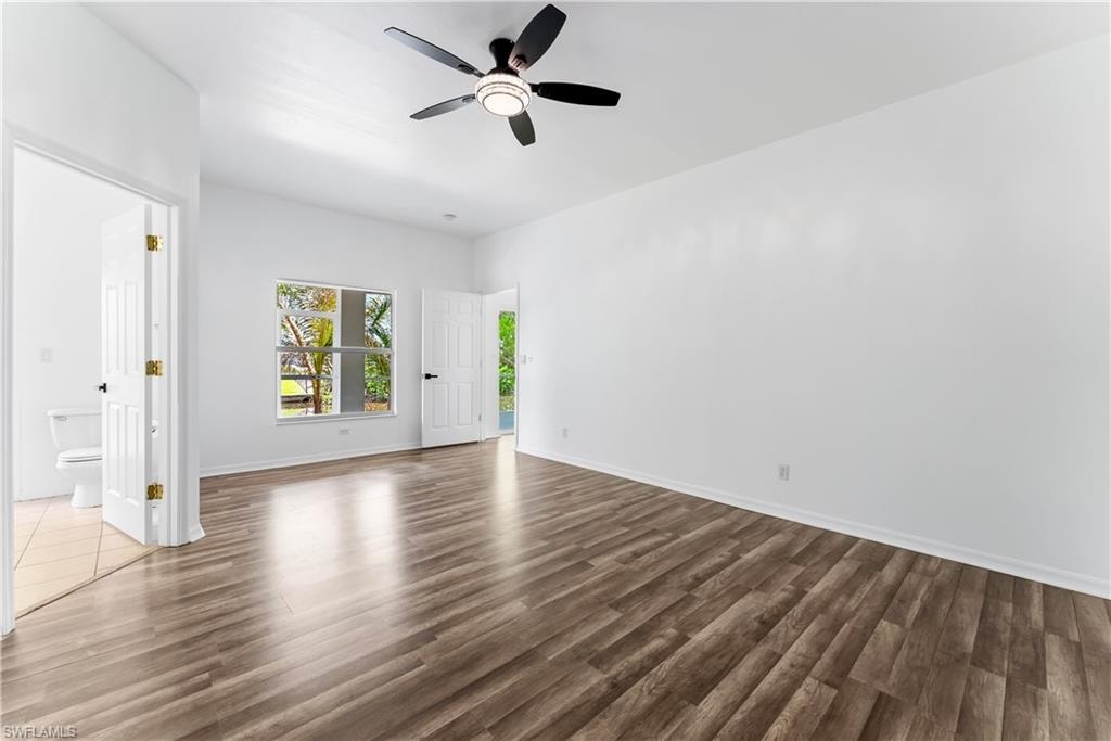 Spacious room featuring wood-finish flooring, a modern black ceiling fan with integrated lighting, and white walls