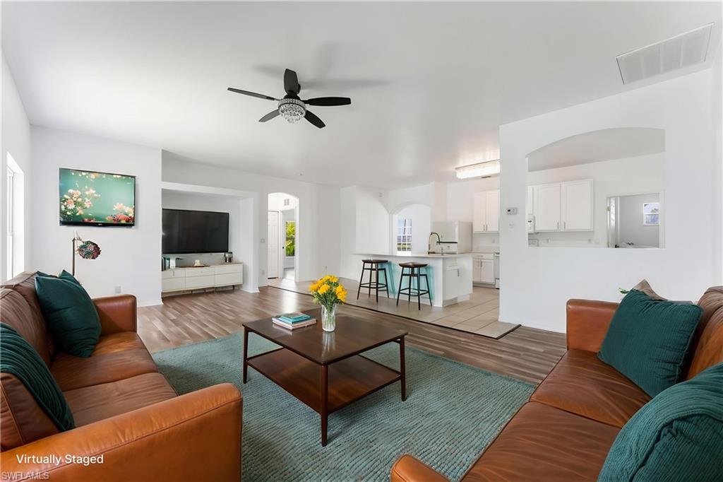 STAGED Bright living area featuring wood-finish flooring, a ceiling fan with light fixture, and an arched entryway