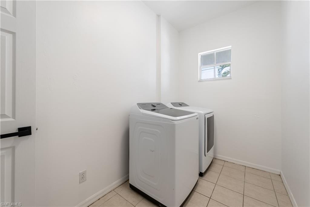 Laundry area featuring light-toned tile flooring, a window providing natural light, and a white paneled door with a matte black handle