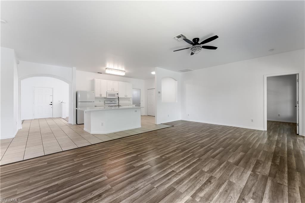 Open-concept living space featuring wood-finish flooring, a white kitchen island with a built-in sink, white cabinetry, and stainless steel appliances