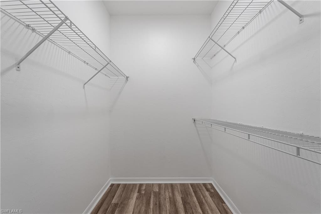 Walk-in closet featuring wire shelving, white painted walls, white baseboards, and wood-finish flooring