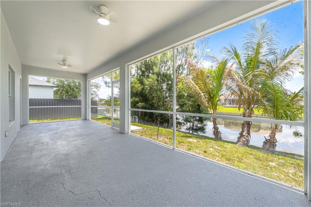 Expansive screened patio featuring two ceiling fans with integrated lighting, a textured concrete floor, and a tranquil water feature beyond the screen enclosure