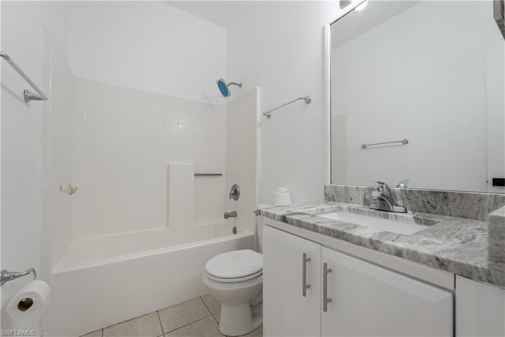 Full bathroom featuring a white tub-shower combination with subway tile surround, a built-in toilet, and a vanity with a light gray veined countertop, an undermount sink, and white cabinetry