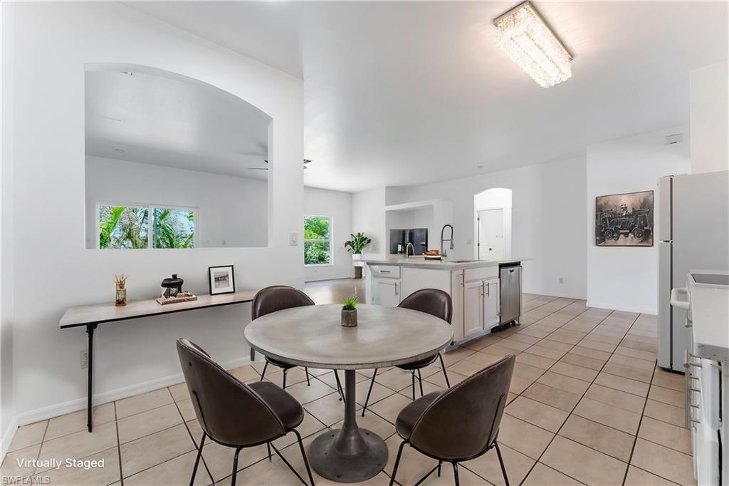 STAGED Open-concept kitchen and dining area featuring a tile floor, white cabinetry, an island with a sink and a stainless steel dishwasher, and a rectangular crystal chandelier