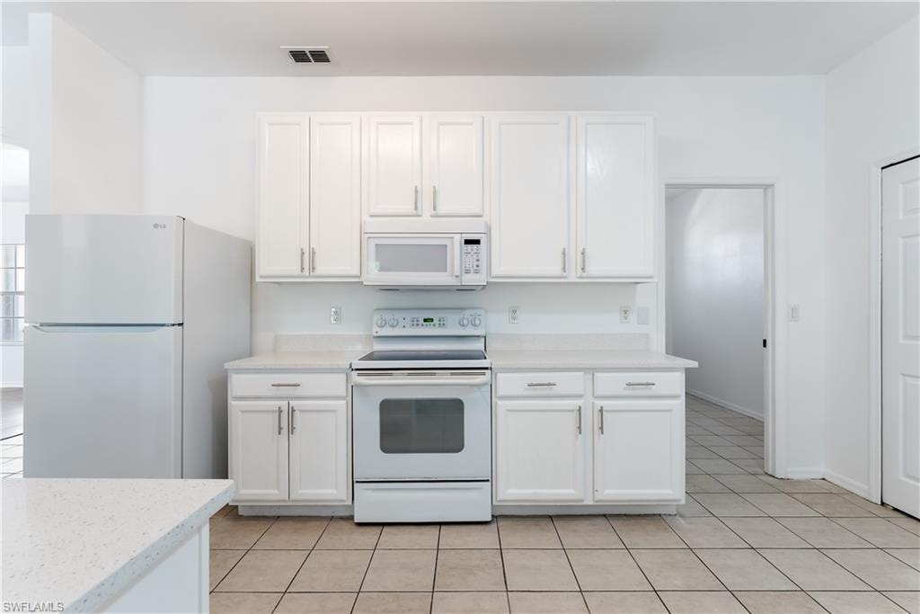 White cabinetry with brushed nickel hardware, speckled countertops, and an integrated white appliance suite