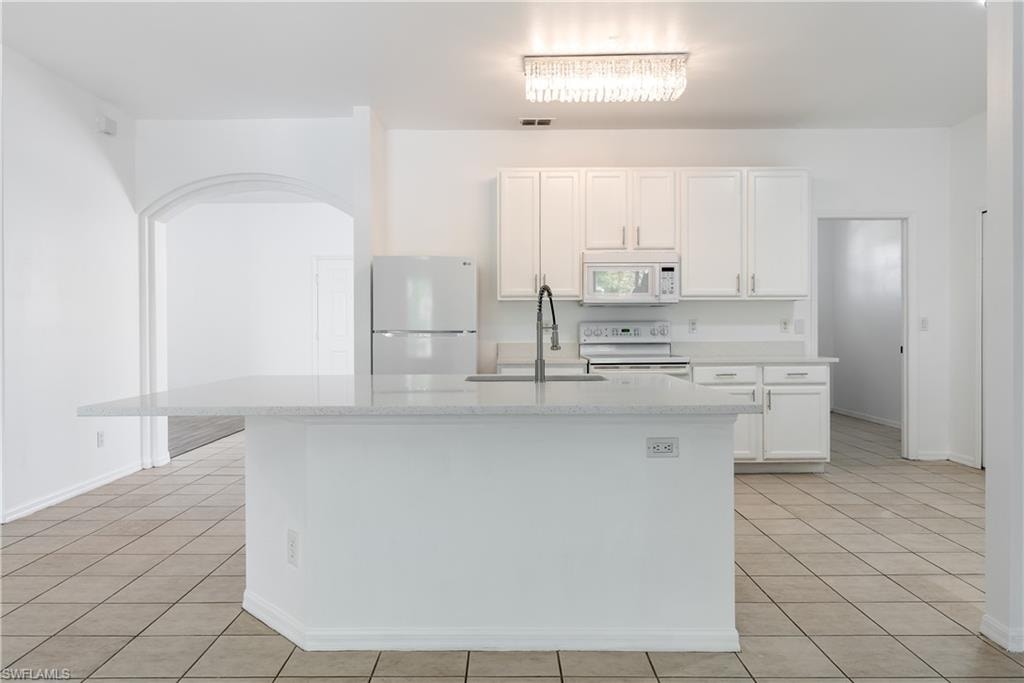 Kitchen featuring a large breakfast bar with light-toned countertop, white cabinetry, integrated appliances, and tile flooring