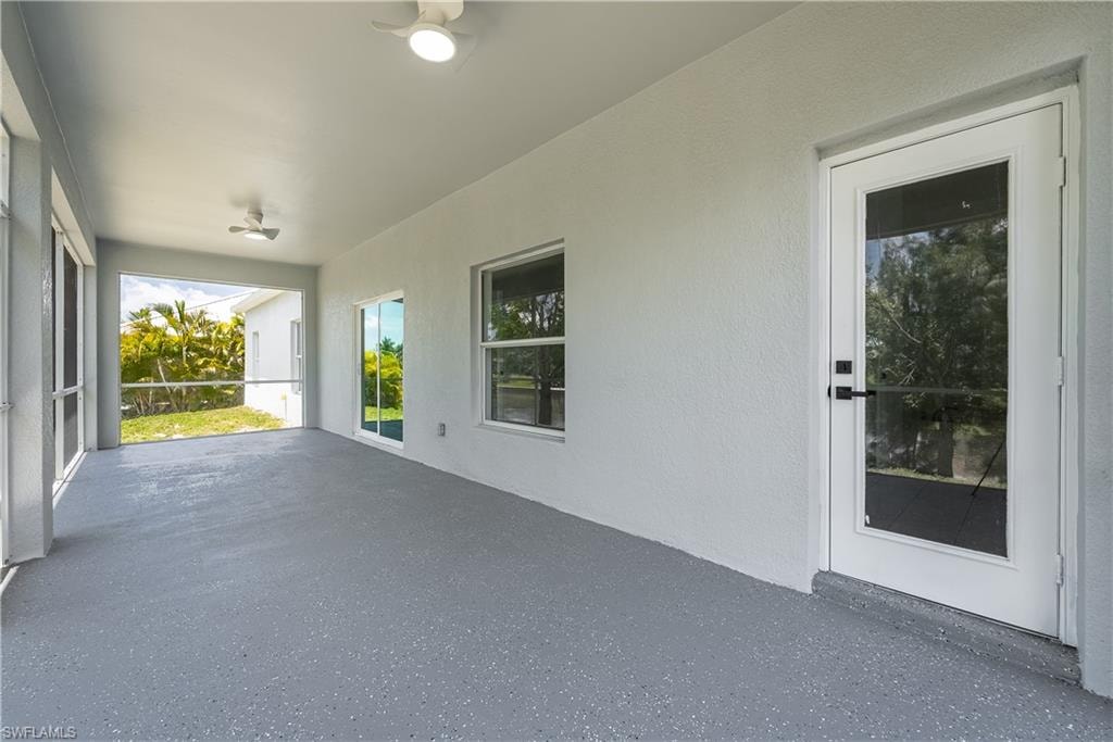 Spacious covered patio featuring a textured floor, white walls, and dual ceiling fans
